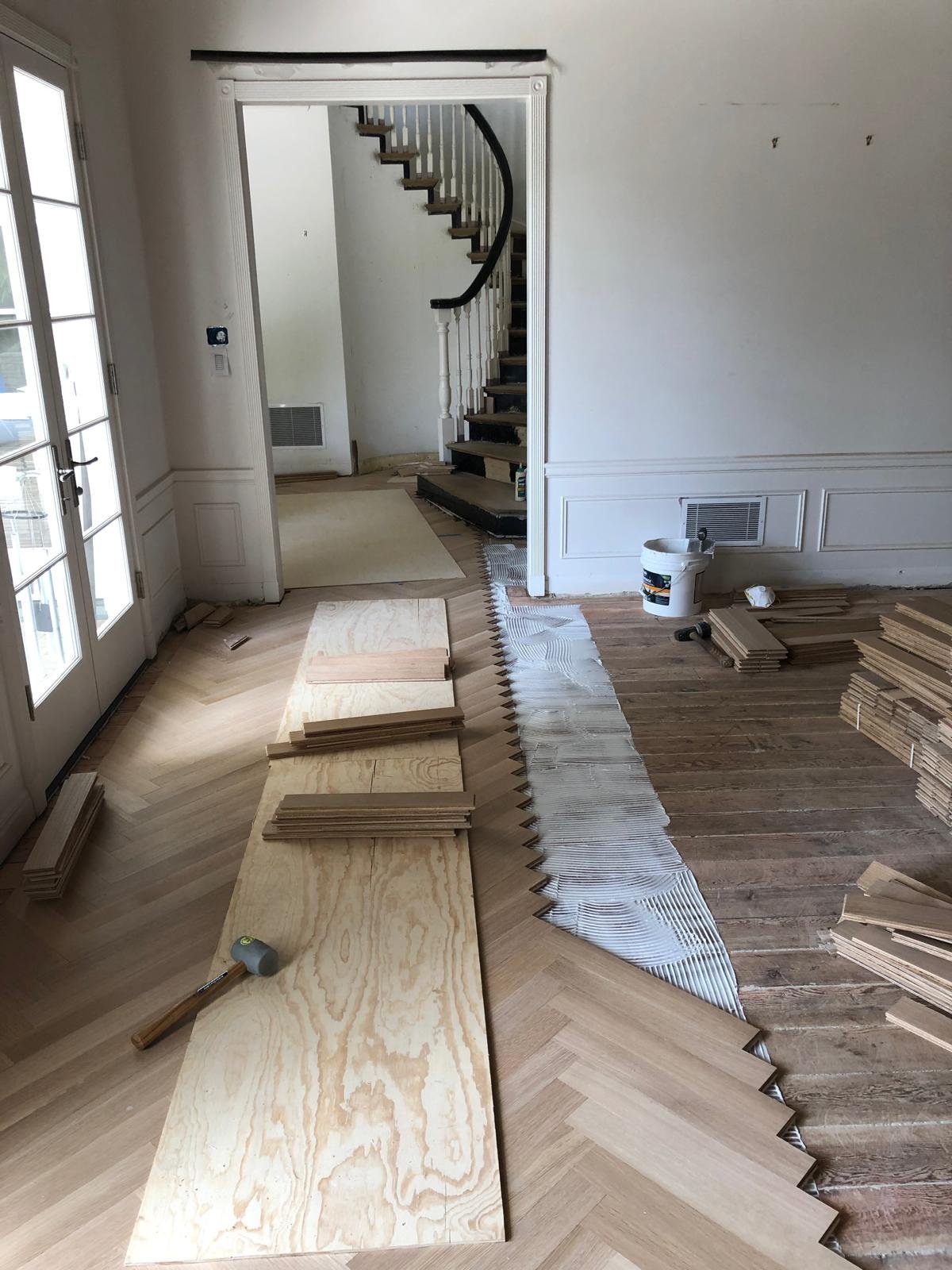 Acacia Wood Floors renovation in progress — herringbone wood floor being installed alongside existing floor with glue-down pattern visible