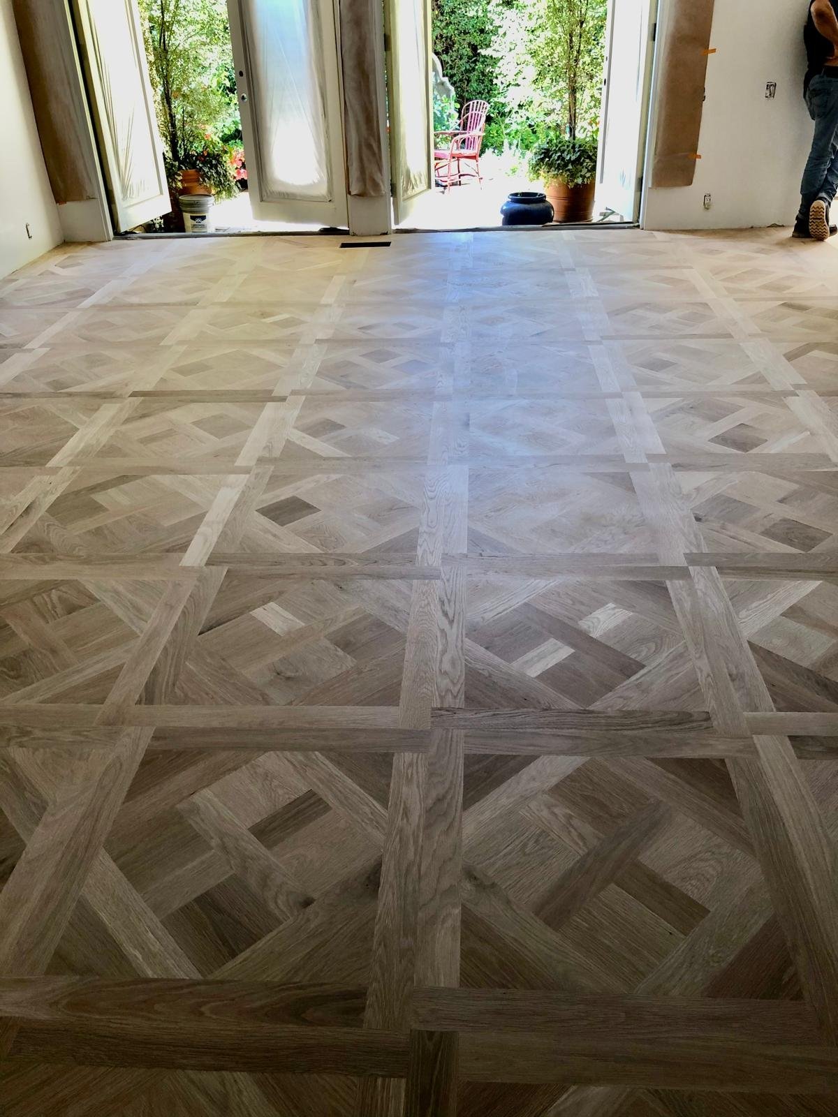 Acacia Wood Floors project — completed custom geometric parquet floor in a spacious room with French doors opening to a green outdoor area