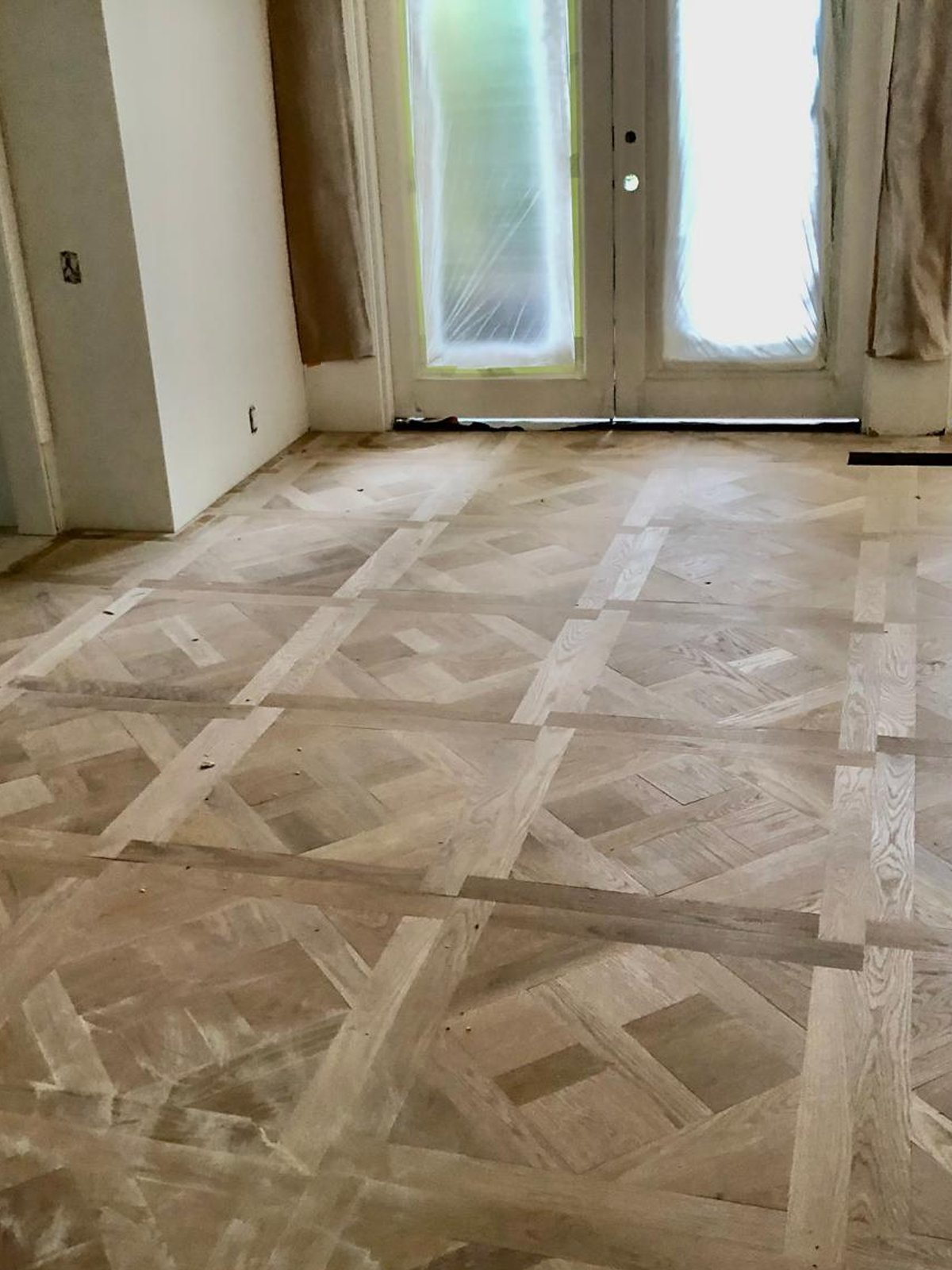 Acacia Wood Floors project in progress — custom geometric basket-weave parquet installation with French doors and natural light