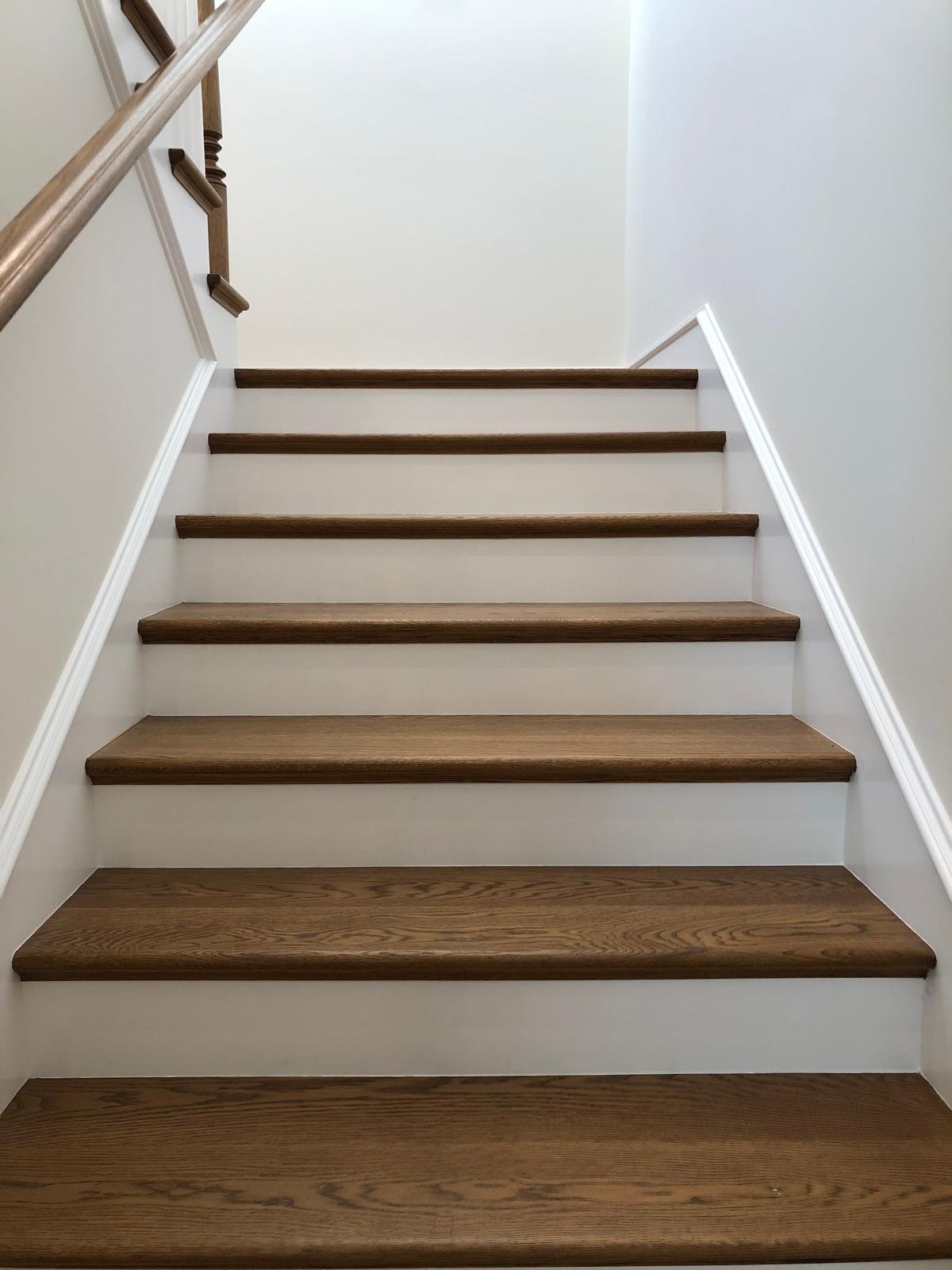 Completed Acacia Wood Floors project — classic oak staircase with warm-stained wood treads, white risers, and white walls