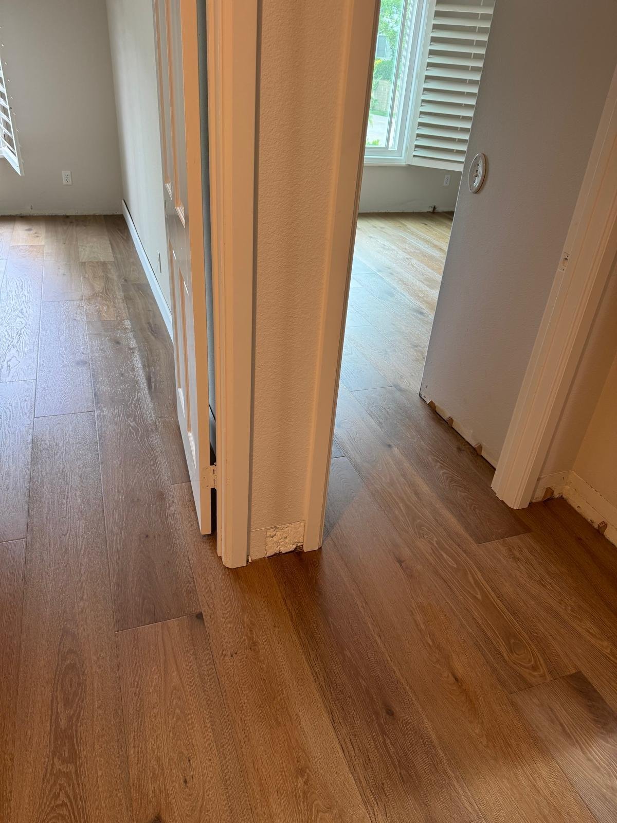 Completed Acacia Wood Floors project — newly installed honey-oak wide-plank hardwood floor flowing through a residential interior, with crisp white door frames, white plantation shutters, and natural light filling the rooms