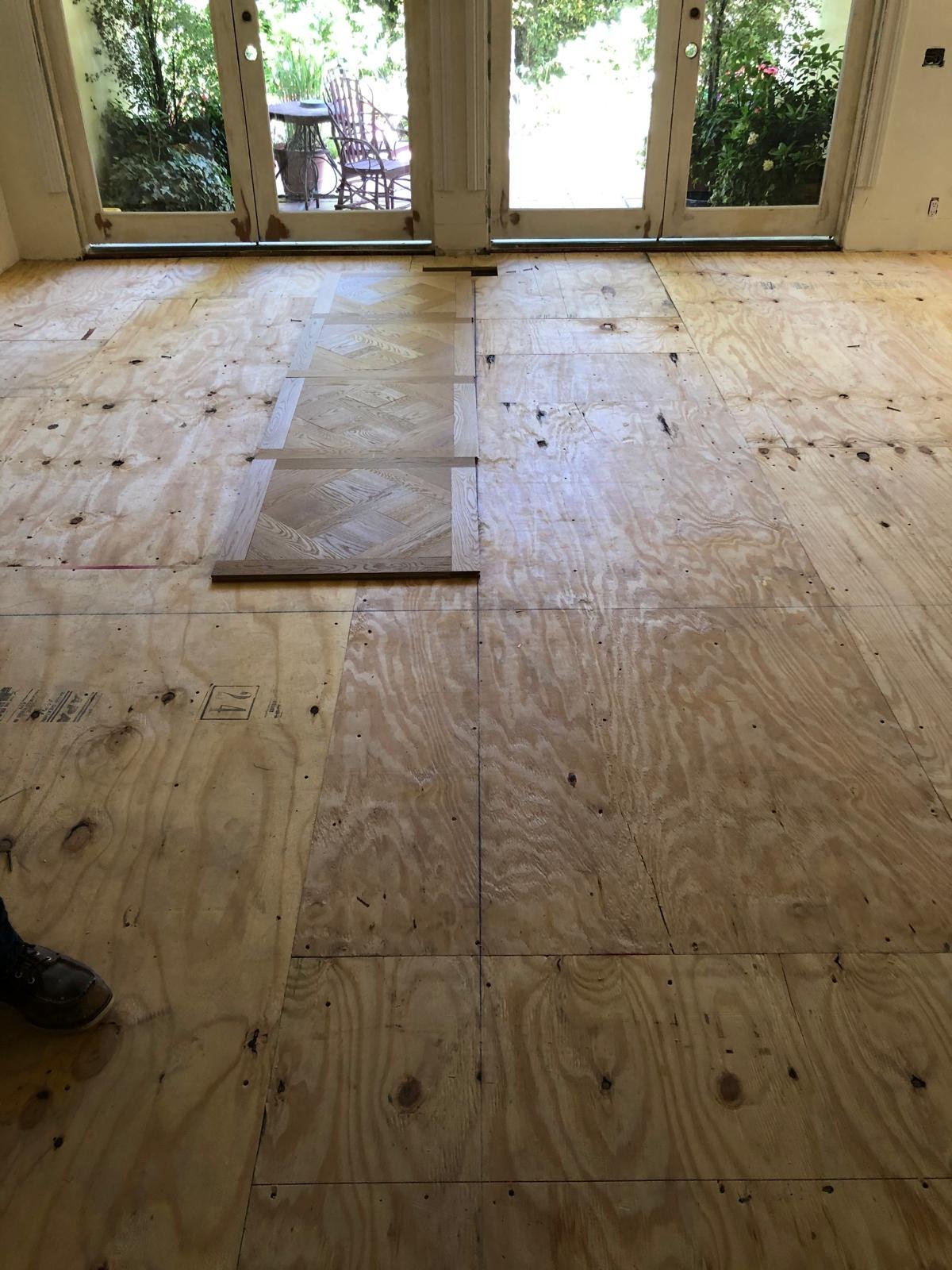 Acacia Wood Floors project in progress — parquet sample laid out on the subfloor before full installation, French doors with natural light