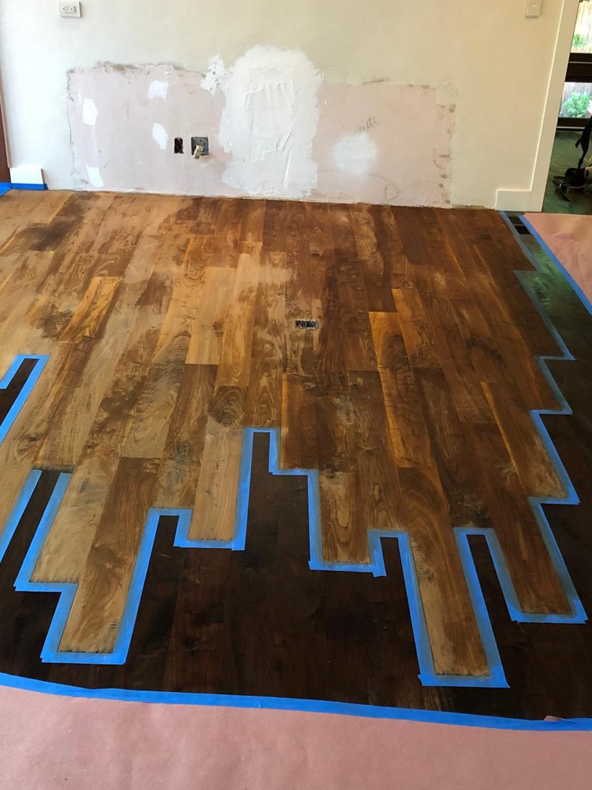 Acacia Wood Floors project in progress — hardwood floor installation with painter's tape marking layout, drywall patches being repaired
