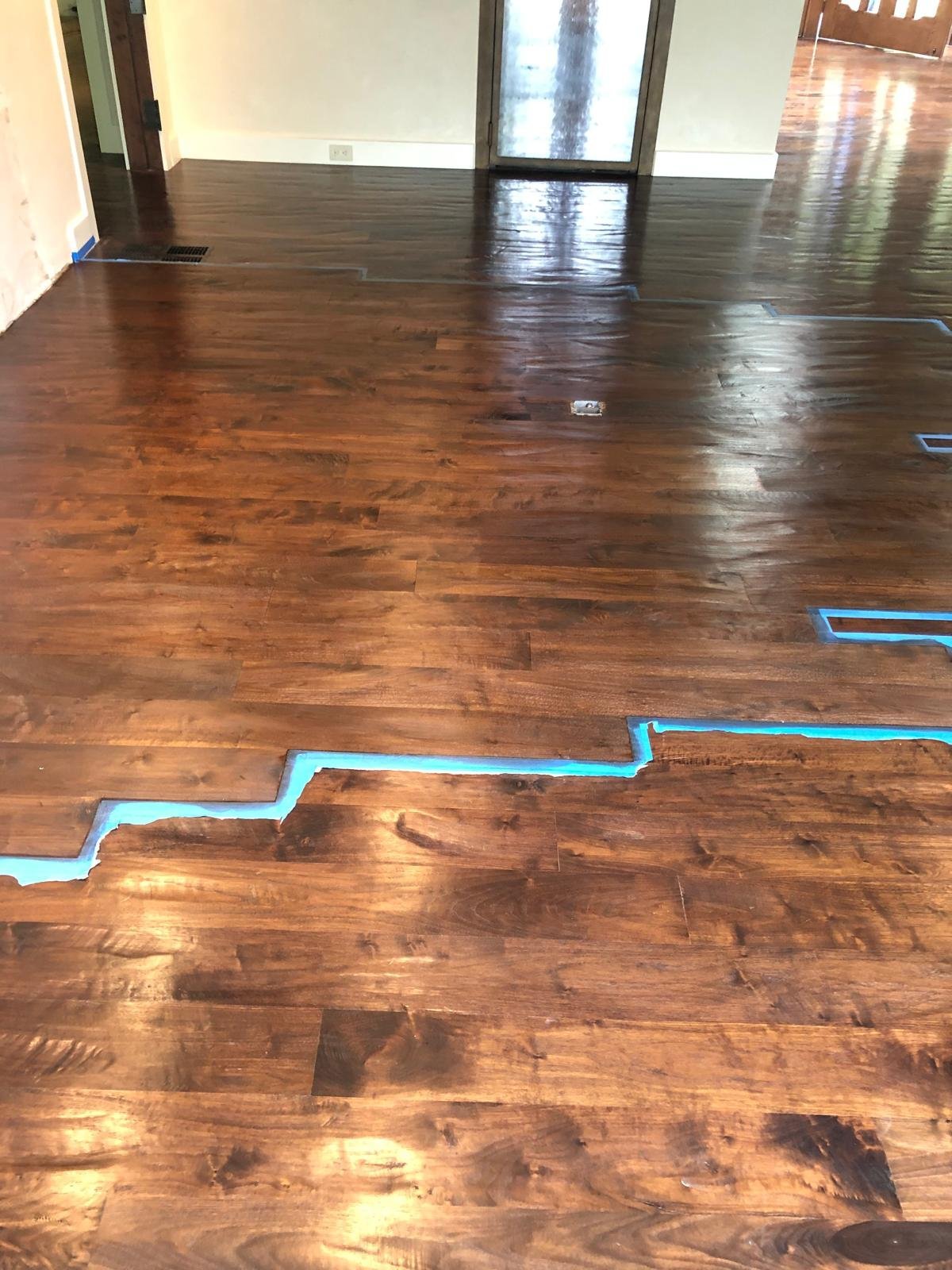 Acacia Wood Floors project in progress — empty room with rich walnut hardwood flooring and blue painter's tape outlining areas during renovation