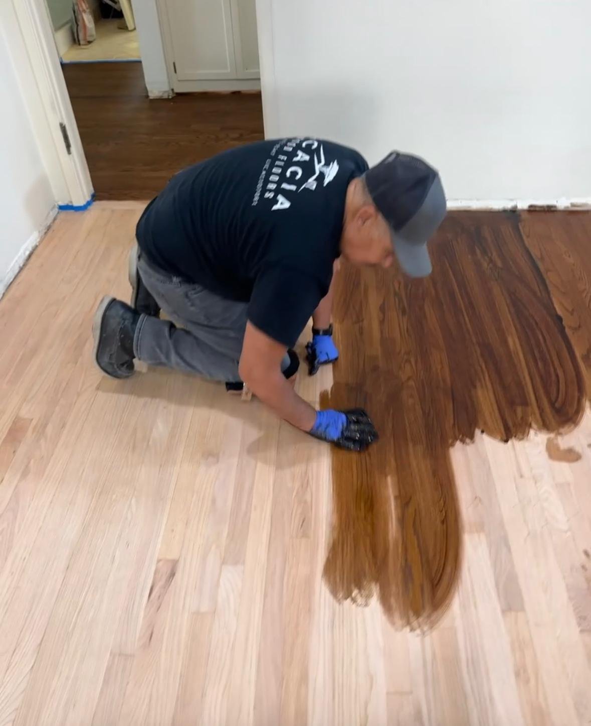 Acacia Wood Floors worker hand-staining a hardwood floor, applying dark wood stain to light-colored planks