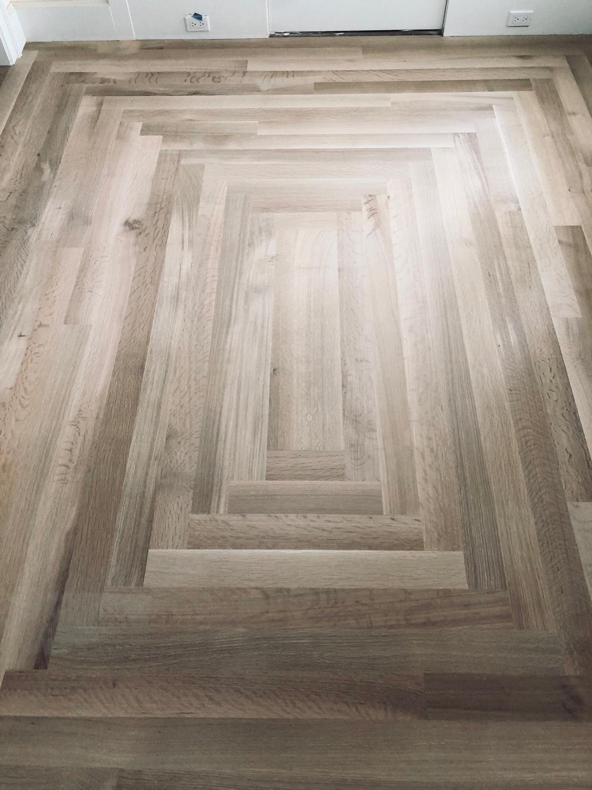 Acacia Wood Floors custom parquet — hand-laid hardwood floor with nested rectangular border pattern in alternating light and medium brown oak tones, creating a concentric frame design